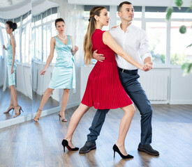 Guy and girl in stage costumes, under guidance of mentor, practice tango in choreographic studio....