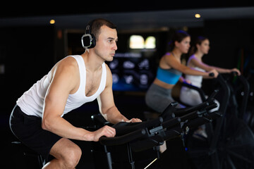 Sportive young man doing spin bike exercises in well-equipped gym during training session