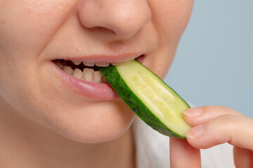 A close-up of a woman biting a cucumber slice, showcasing fresh and healthy eating.