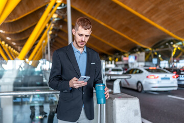 Businessman using smartphone and holding reusable coffee cup at airport