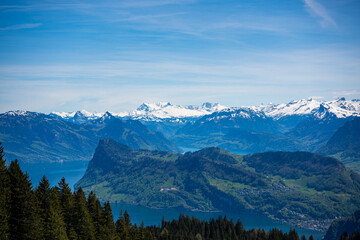 A stunning high-altitude perspective from Mount Pilatus, with snow-capped peaks, lush greenery, and an expansive blue lake in the Swiss Alps. A dream spot for explorers and photographers.
