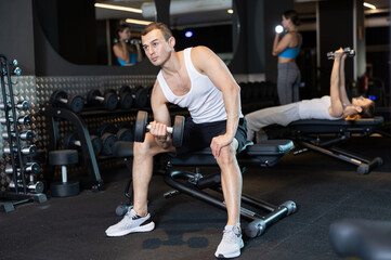 Strong young man practicing with dumbbell in exercise room during weight training