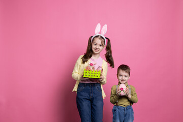 Sweet children holding festive easter decorations on camera, posing with confidence and feeling happy about spring festivity. Brother and sister showing their handmade craft of april ornaments.