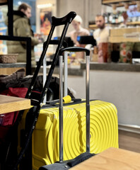 Yellow and black suitcases stand next to a wooden table and black crutches of a passenger with a...