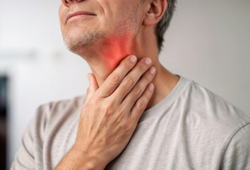 Fototapeta premium A person gently holds their neck, indicating discomfort and showing signs of neck and throat pain. The focus is on self-care and relief strategies at home