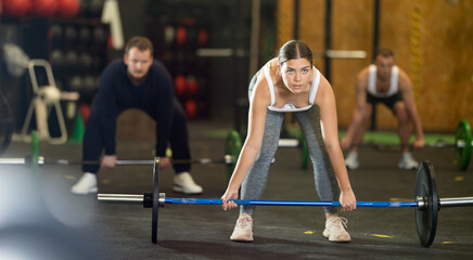Determined young girl working out with barbell in well-equipped gym during training session