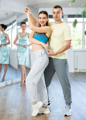 Smiling couple, woman and man in sportswear dancing sensual Latin dance bachata under female instructor watchful eye in choreography studio. Active lifestyle of adults