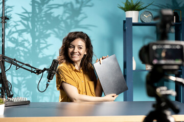 Happy woman in home studio films sleek laptop video review for tech enthusiasts. Cheerful internet...