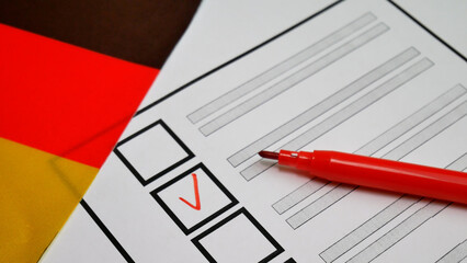 Political choice in Germany. Voters hand votes with red marker, placing checkmark in checkbox. German flag colors in background. Symbolizing fair elections, democratic participation