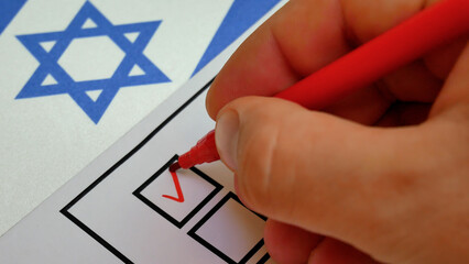 Hand marks choice with red marker on ballot. Democratic elections in Israel. White and blue flag...
