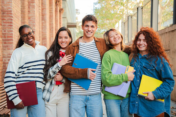 Group of high school friends, standing together at university campus smiling and expressing pure delight and youthful friendship. Real teenage students looking at camera celebrating their bond