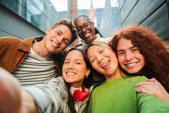 Group of diverse young friends smiling and taking a selfie together, showcasing joy and happiness. Five multiracial teenage students having fun taking a portrait, laughing looking at camera