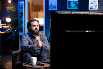 Man relaxing at home on couch, being gripped by suspenseful films shown on television screen. Person streaming content in neon lit living room, fascinated by entertaining movie scene