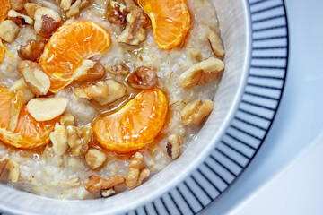 Hot and creamy oatmeal breakfast cereal in bowl topped with juicy mandarin orange sections, chopped walnuts and drizzled with manuka honey
