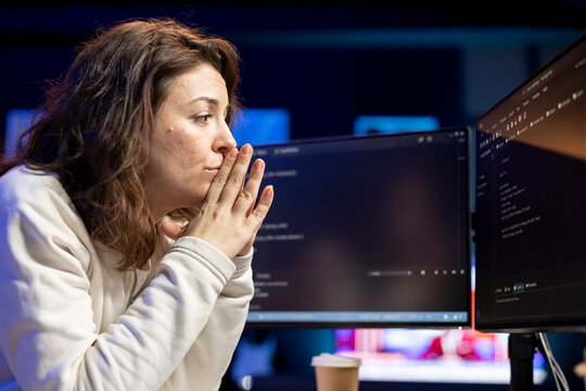 Pensive woman developing software in Java programming language using desktop PC, examining. Contemplative programmer in apartment thinking how to solve coding issues on computer
