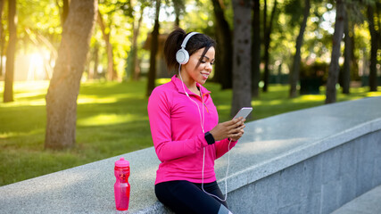 Black girl jogger using sport app for smartphone while resting during training in public park, empty space