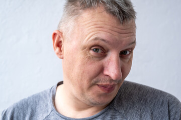 Obraz premium Portrait of a cheerful middle-aged man wearing a gray hoodie, standing against a textured stone wall in natural light.