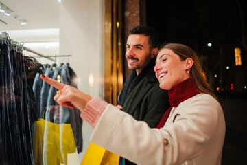 Happy couple admiring a storefront display at night, shopping together with stylish clothing options, reflecting excitement, curiosity, and bonding during a relaxed and joyful evening in the city