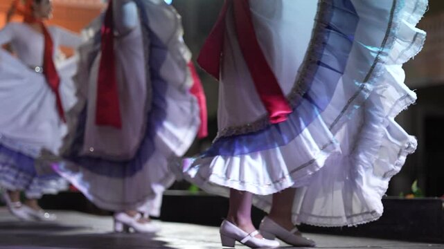 Women dance gracefully in a vibrant dress, showcasing folk traditions of Nicaragua and Mexico during a captivating cultural performance at night.