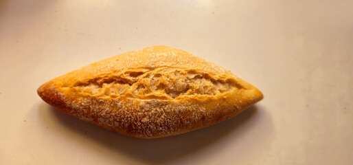 Golden brown bread roll with a crisp crust and a symmetrical slash pattern on top; placed on a smooth, light-colored surface with soft lighting;