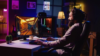 Man arriving in gaming room, ready to play science fiction videogame on PC with his friends. Gamer using headphones microphone to talk with internet teammates in online coop shooter