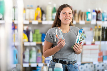 Young woman buyer chooses toothbrush in household chemicals store