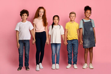 School friendship. Adorable multiethnic children holding hands together on pink background