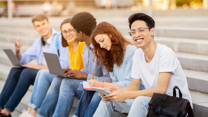 Teamwork Concept. Multiethnic students sitting on steps and learning, asian boy looking at camera