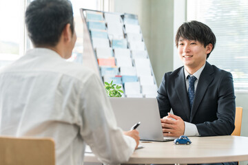 男性客と商談・接客・打ち合わせする若いアジア人ビジネスマン（自動車・保険）
