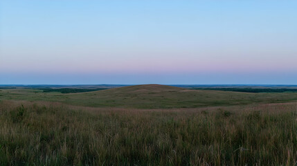 Fototapeta premium Rolling green hills of a vast prairie landscape under a soft pink and blue twilight sky at dusk.