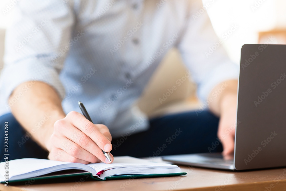 Poster note taking. closeup of unrecognizable male person using laptop, writing in notebook, blurred backgr