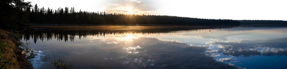 Panoramic view of a calm lake reflecting clouds with partially transparent sky
