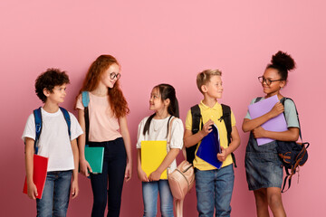 Cute schoolkids of different races and ages looking at each other over pick background