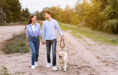 Fototapeta premium Bonding Concept. Two laughing people holding hands, spending time outdoors with their puppy, sun flare light