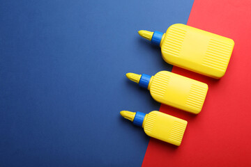 Bottles of glue on color background, flat lay. Space for text