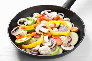 Frying pan with mix of vegetables and mushrooms on white wooden table, closeup