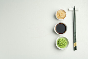 Hot wasabi paste, soy sauce, ginger and chopsticks on light textured table, flat lay. Space for text