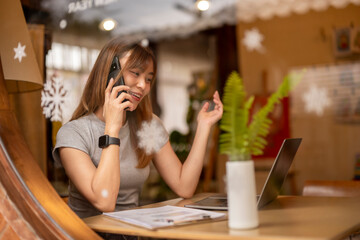 A woman is talking on her cell phone while sitting at a table with a laptop