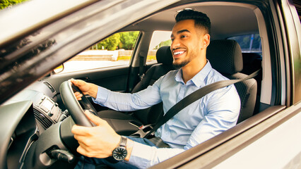 Naklejka premium Right-hand drive auto concept. Positive middle-eastern guy in formal outfit going to office, driving car, happy arab businessman enjoying his new luxury automobile, shot from outside