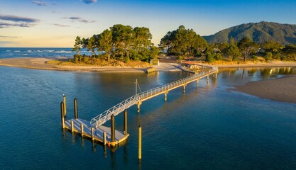 Obraz premium Aerial view of a scenic Pauanui boat ramp pier, with people using the walkway. Tranquil coastal scene at sunset, Coromandel Peninsula, New Zealand