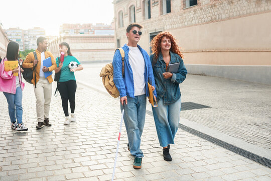 Happy blind man walks with group of friends inside school or university campus. People students, education concept