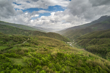Rolling hills of green forest under a cloudy partially blue sky create a picturesque mountain view