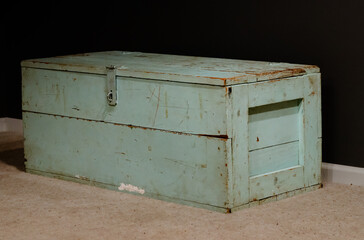 An old green army trunk sitting in the corner of a room