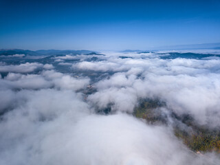 Fototapeta premium Aerial view of fluffy clouds blanketing a landscape with blue sky and distant mountain ranges