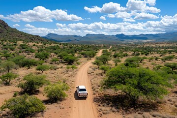 Obraz premium White Truck Drives Through the Arid Landscape of Namibia Under a Vast Blue Sky and Clouds