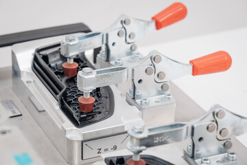 A metal jig with clamping tools secures a black plastic component for precise manufacturing or inspection