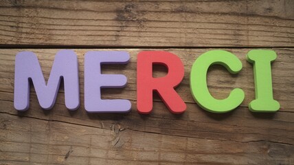 Fototapeta premium Colorful block letters spell merci on a rustic wood surface