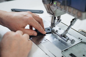 Hands guiding fabric under the needle of an industrial sewing machine in a bright professional workspace