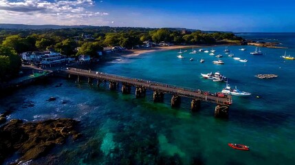 Fototapeta premium Wide Aerial View of Coastal Pier Stretching Into Blue Ocean Under Clear Sky
