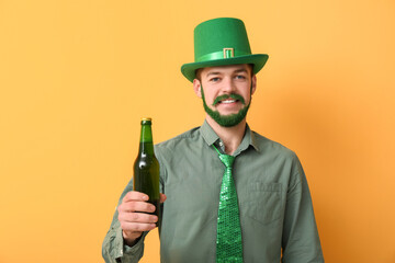 Young man in leprechaun hat with green beard holding bottle of beer on yellow background. St....